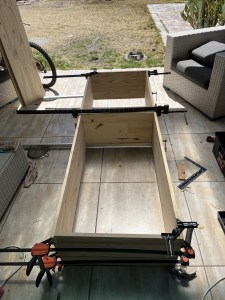 The frame of a pine bookshelf rests in clamps