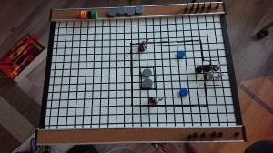 A whiteboard with a 1inch grid and small tokens making up a gameboard.