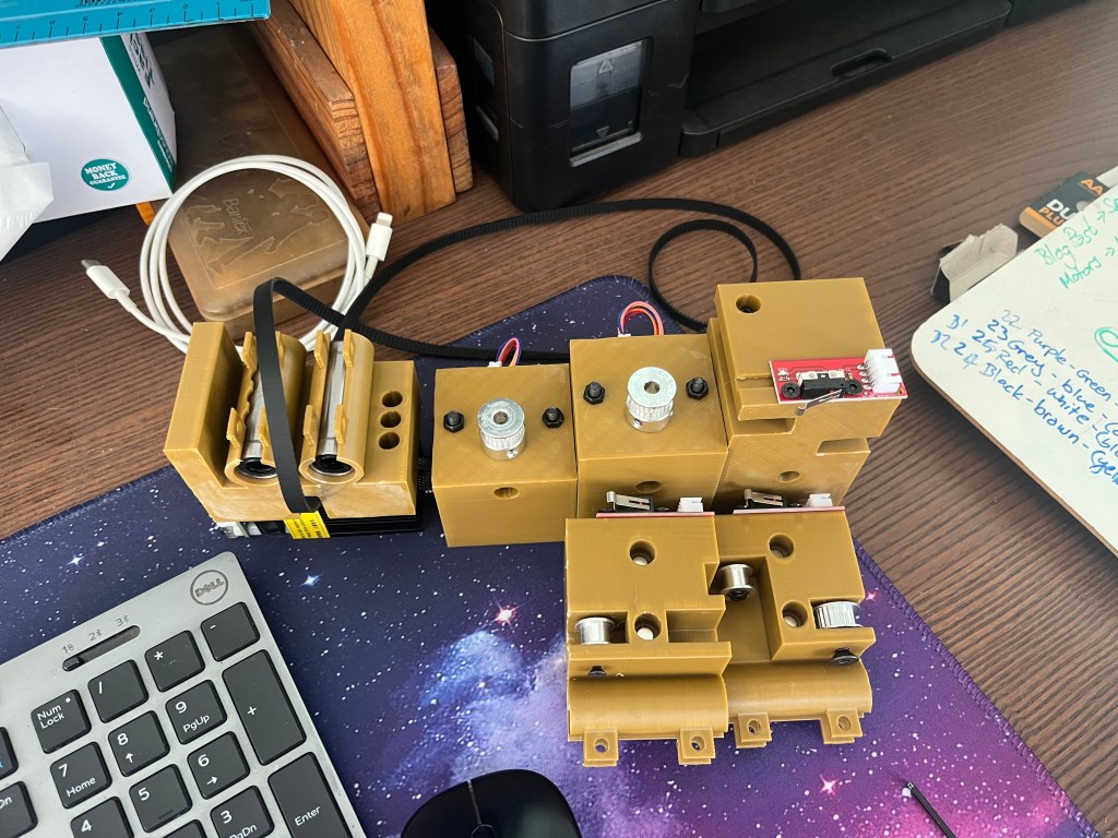 A close-up view of a partially assembled laser engraver, featuring various 3D printed components, wiring, and electronics, placed on a desk.