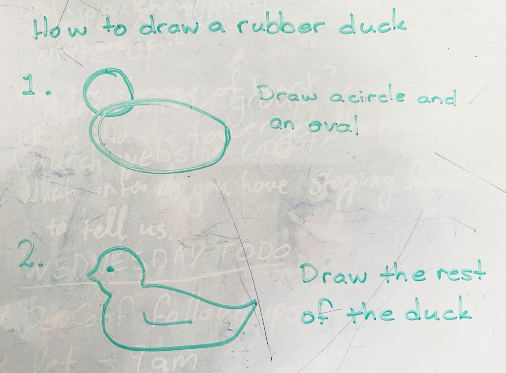 A marker-on-whiteboard drawing, copying the "how to draw an owl" meme, it says "How to draw a rubber duck" followed by unhelpful instructions.